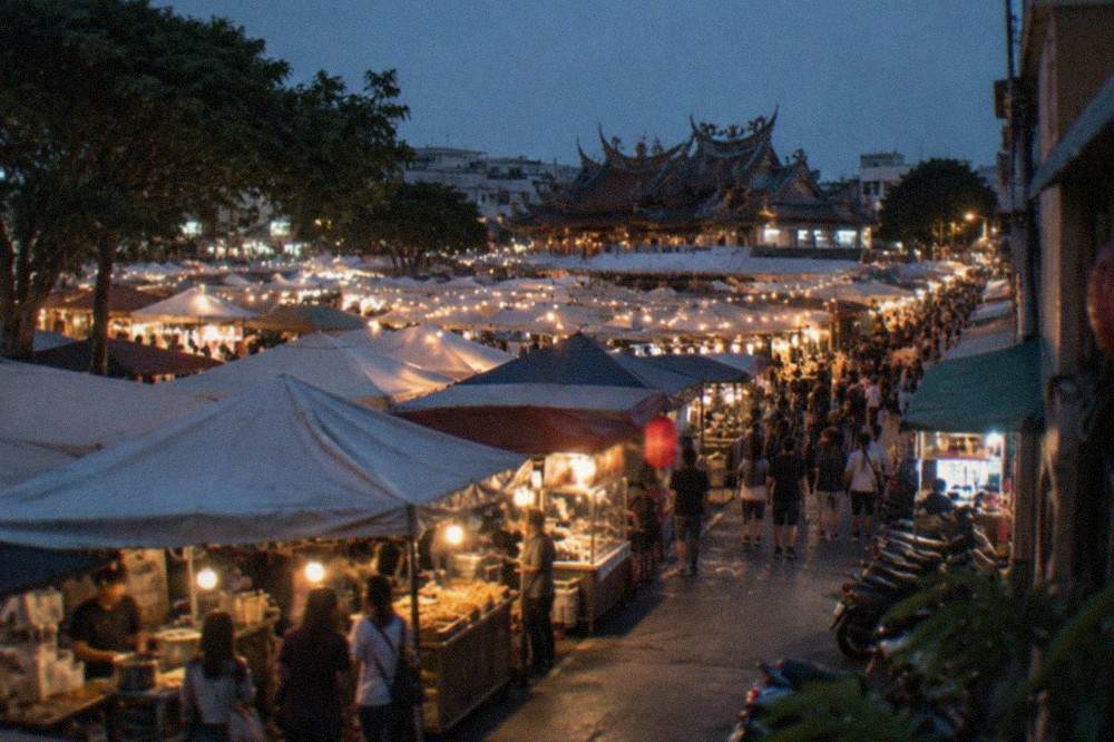 A night market lane in Tainan lit by stall lights with crowds browsing food stands