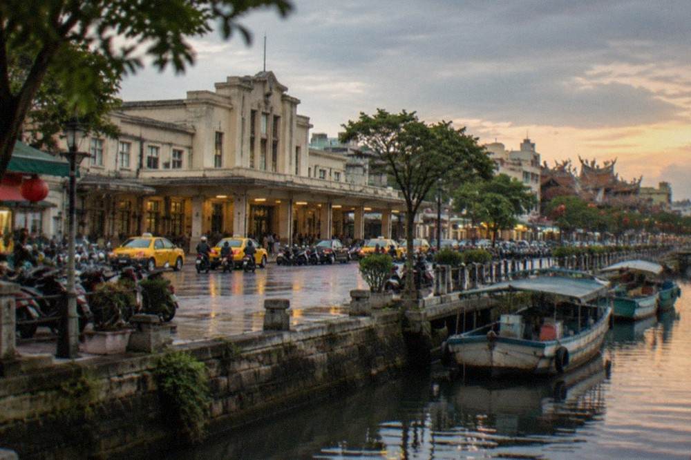 A Tainan canal at dusk with boats moored along the bank