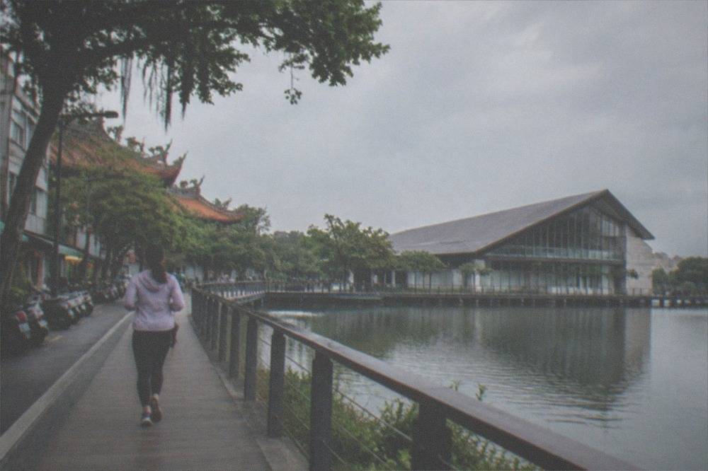 A modern museum building with a large sloping roof beside a calm lake and boardwalks