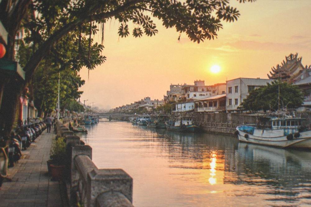 Sunset light over Anping Canal with moored boats and a waterfront walkway