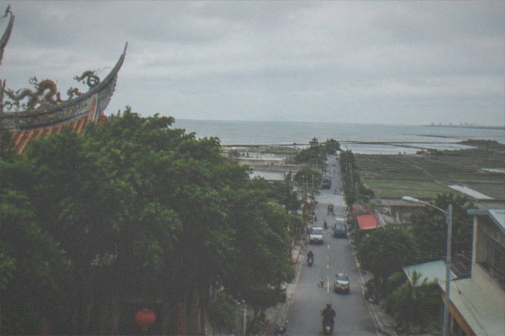 A narrow road running straight across flat coastal farmland toward distant water