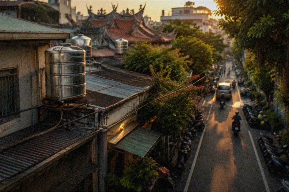 Evening light across low Tainan rooftops, water tanks and power lines, the street below falling into shadow