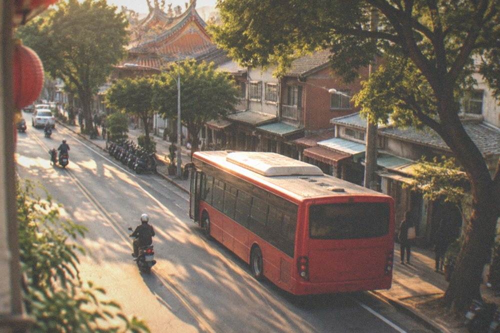 A red city bus at a stop on a tree-lined Tainan street in late afternoon