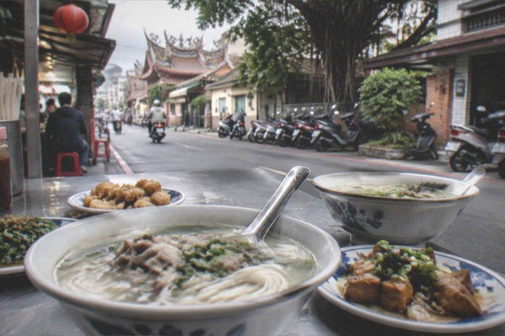 Bowls of noodle soup and small plates on a table at a busy Tainan food stall