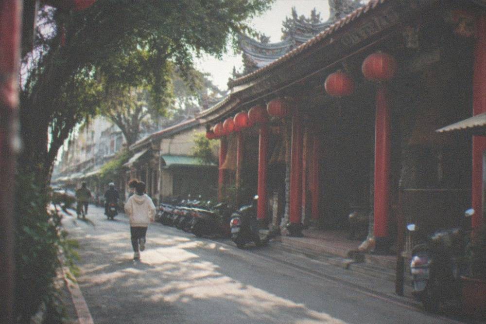 A small neighborhood temple with red pillars, lanterns hanging from the eaves and incense coils