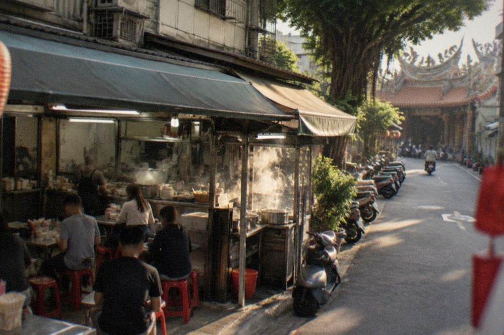 A small Taiwanese noodle shop at night with steam rising from cooking pots and customers seated on plastic stools