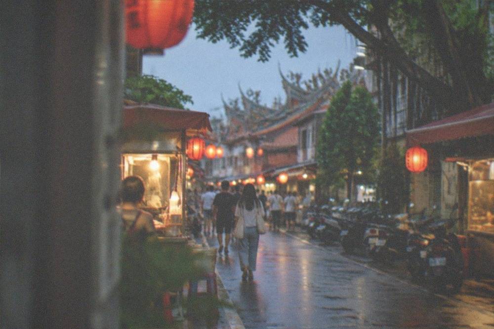A lantern-lit Taiwanese street at dusk with food stalls and people walking between them