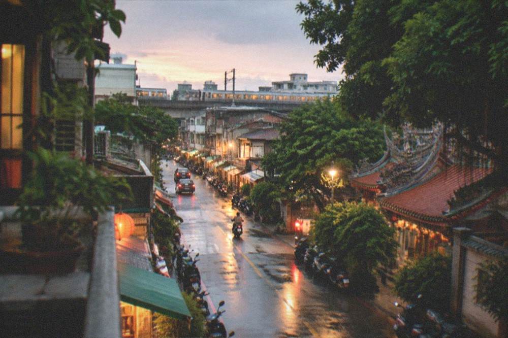 An evening view over a Taiwanese district with warm window lights and a distant railway line