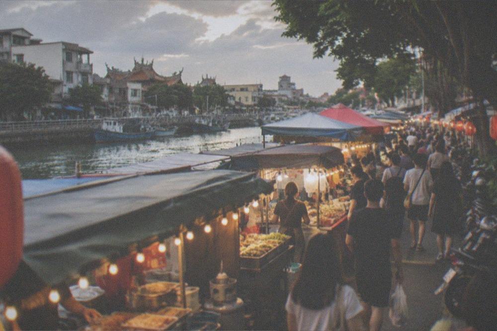 A crowded night market aisle lit by strings of bulbs, with food stalls and customers on both sides