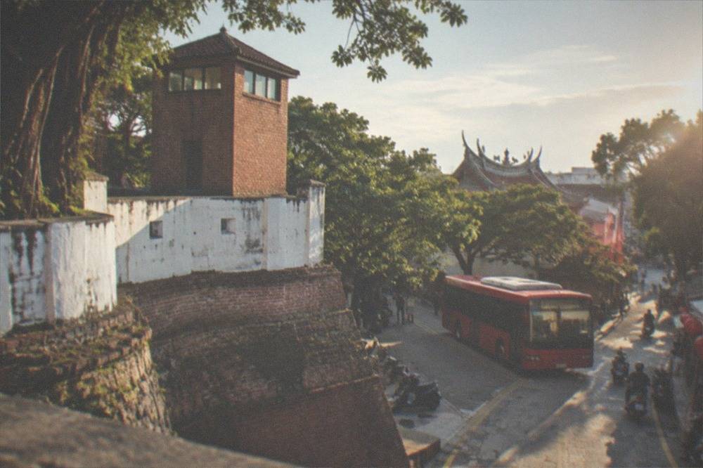 A red-brick city bus stopped at a sunny street in an old Taiwanese district