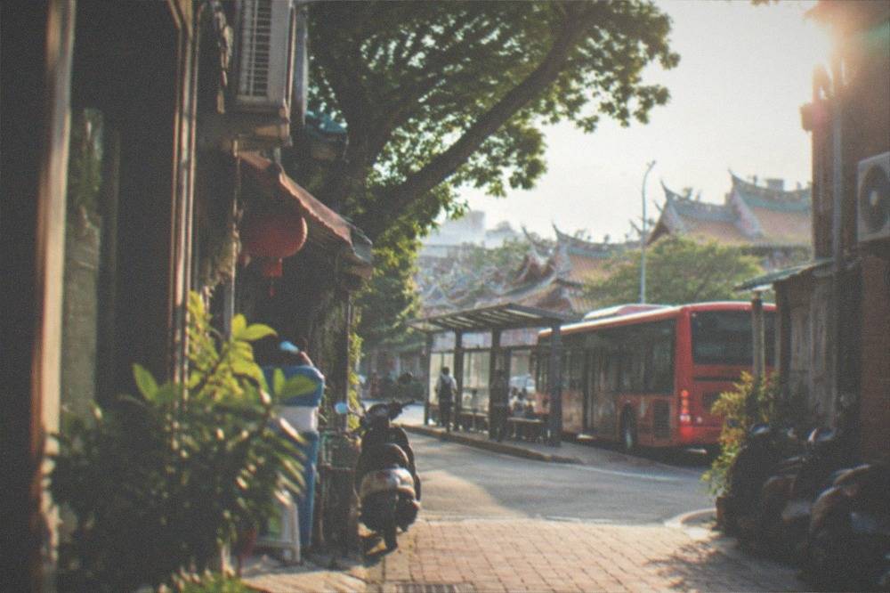 A red city bus stopped at a sheltered bus stop on a Tainan street