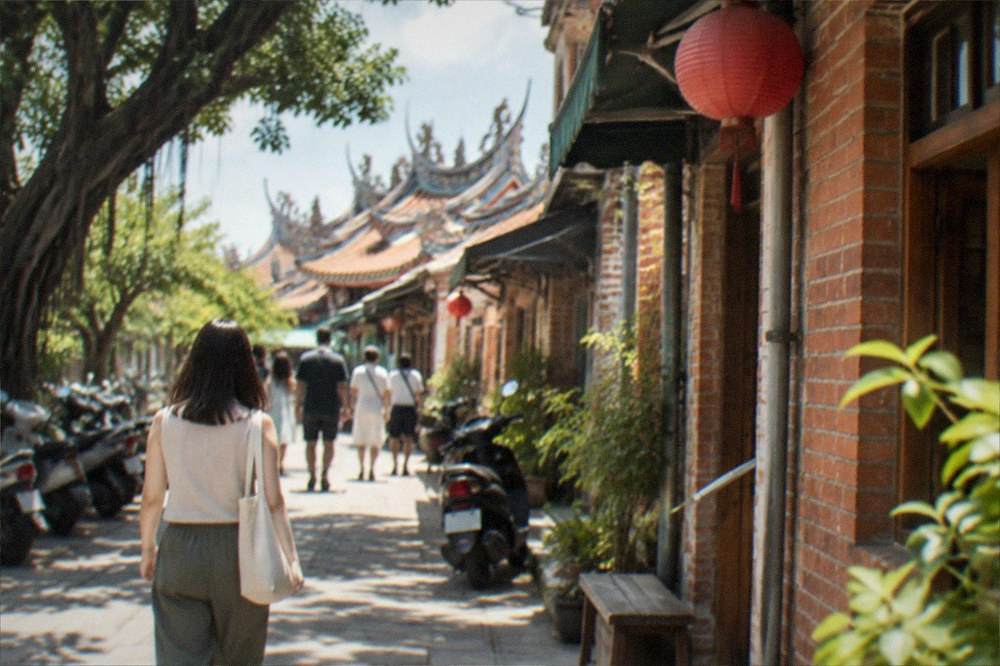Visitors walking a sunlit Anping lane lined with old brick houses and small shops