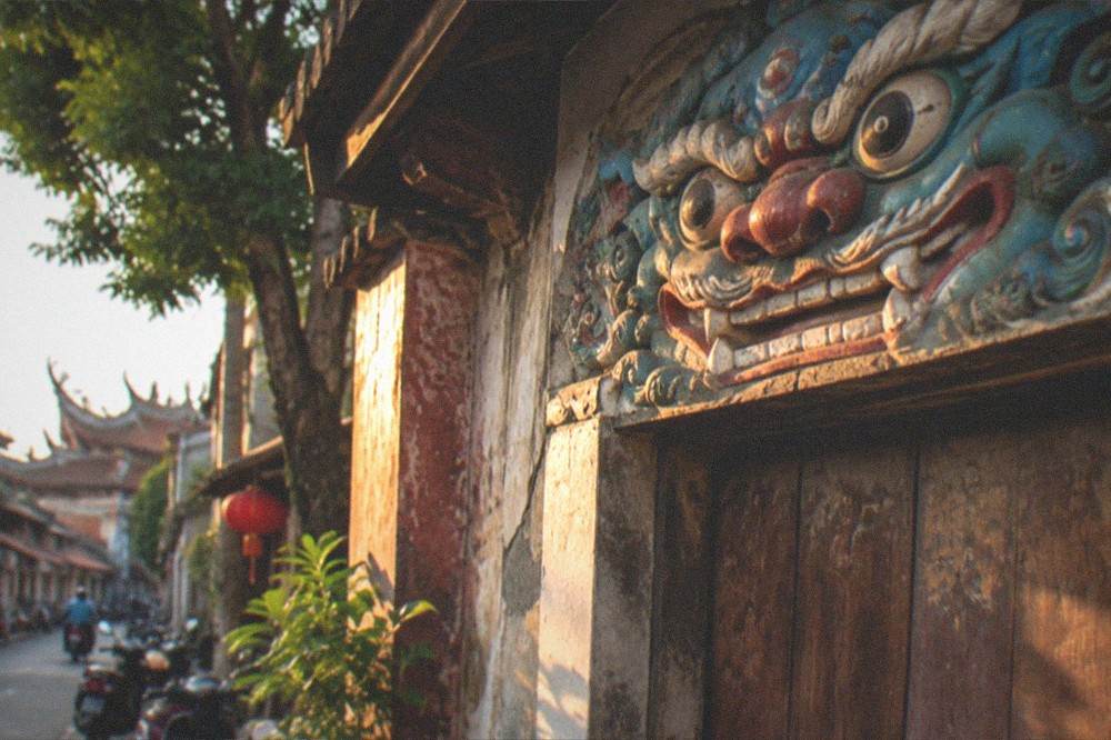 A close view of a painted sword lion face above an old wooden door in Anping at golden hour