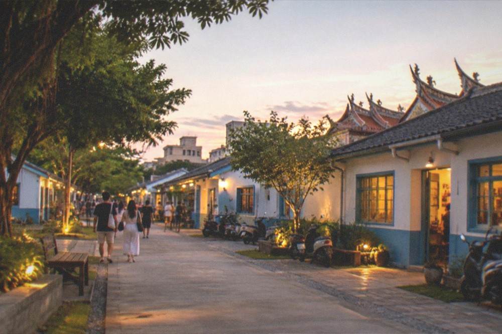 A wide view of a creative park at dusk with warm lights along walkways and people strolling
