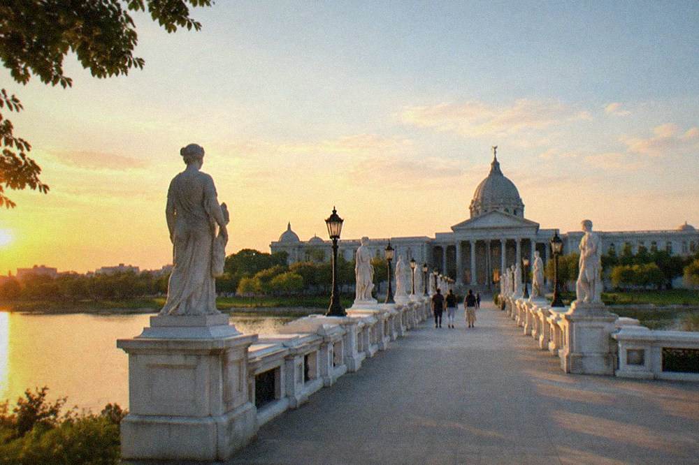 The Olympus Bridge walkway lined with statues leading across the lake to the museum entrance