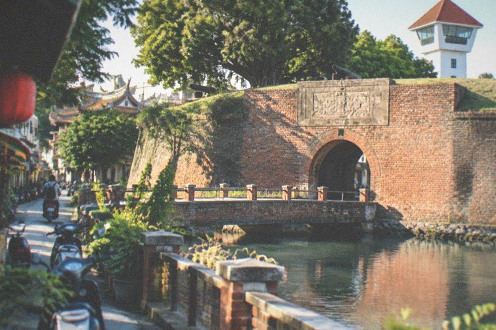 A brick gate arch with a weathered carved stone panel above it, the carving seen at a raking angle so no characters read