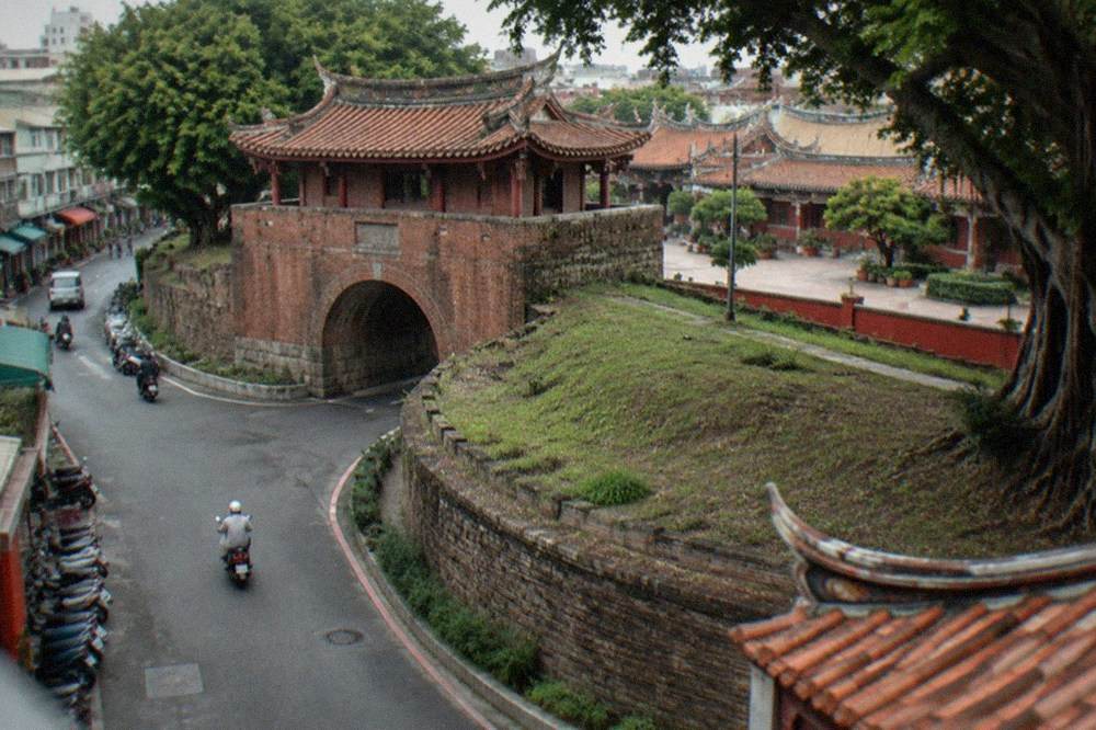 A temple courtyard with red walls and low tiled roofs in warm afternoon light