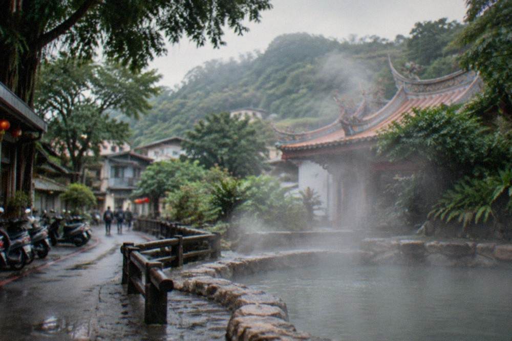 Steam drifting over an outdoor stone bathing pool surrounded by trees