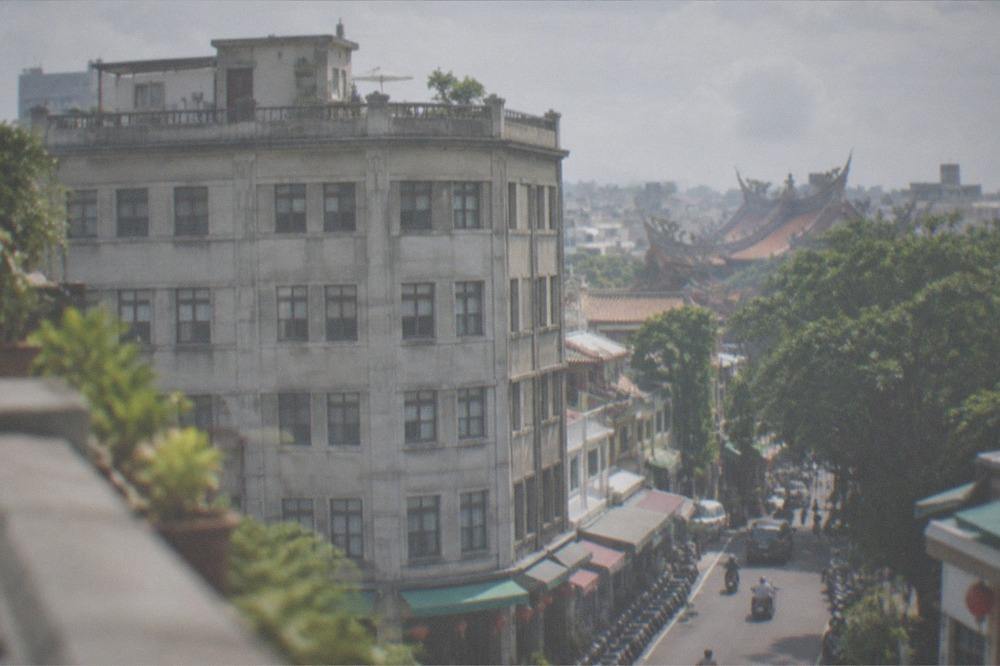 A rooftop terrace overlooking tiled rooftops and temple rooflines under a partly cloudy sky