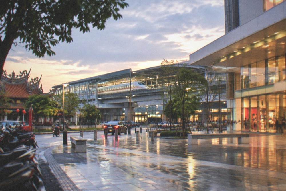 An evening view of a lit mall exterior with the high speed rail station visible beyond it