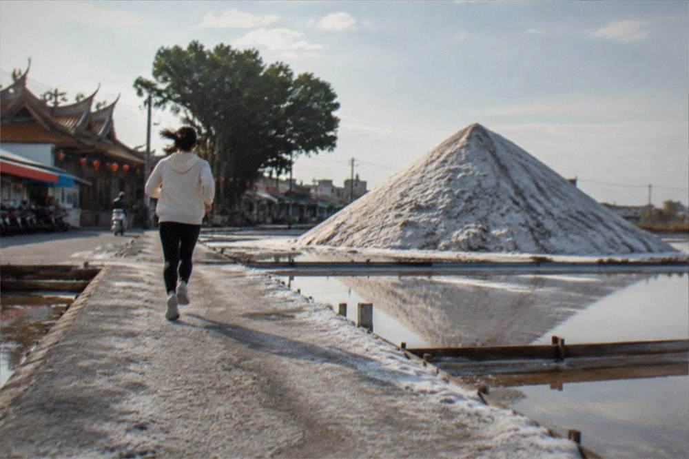 A white salt mountain rising behind shallow salt pans under a wide sky
