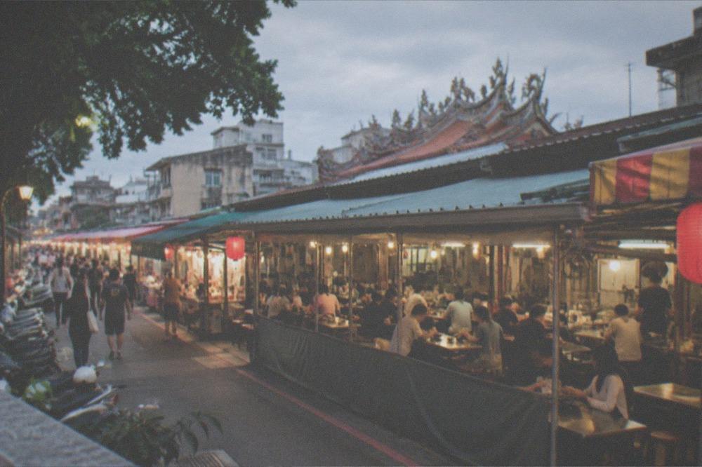 People eating at small tables inside a covered night market in the early evening