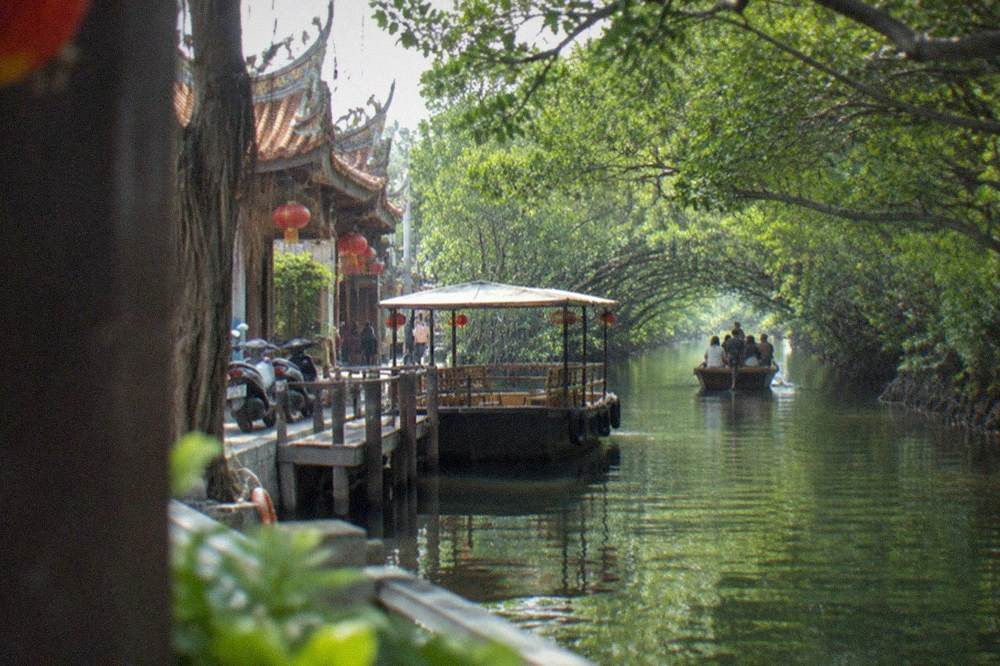 A covered flat-bottomed tour boat moored at a wooden pier beside a temple