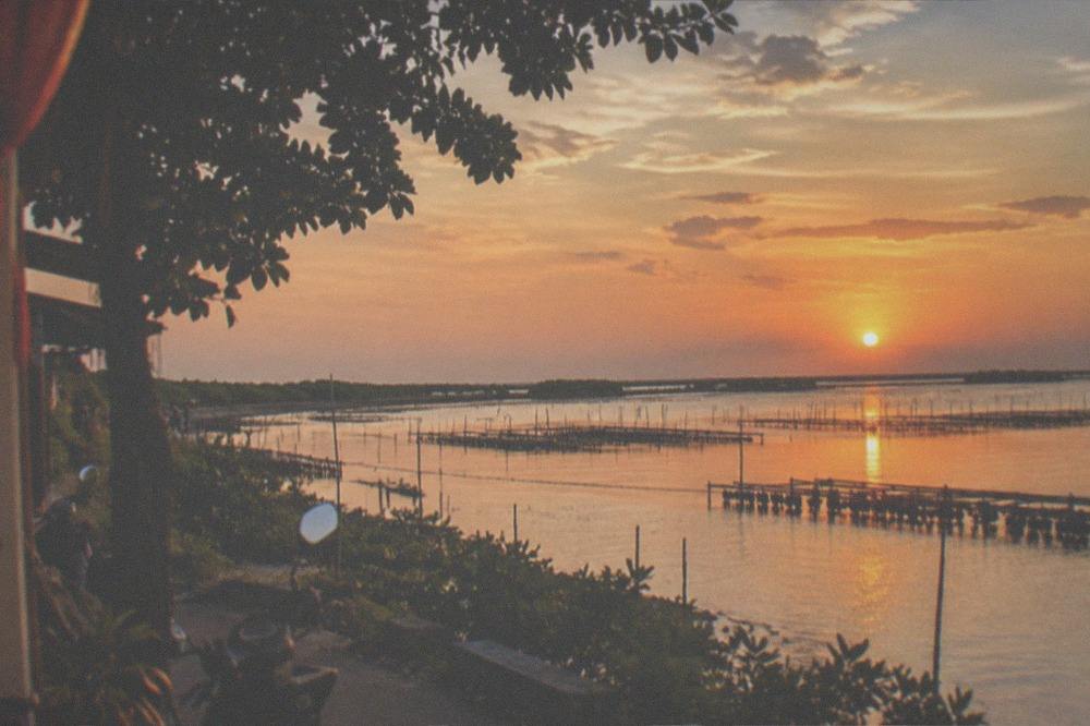 Sunset over a coastal lagoon with silhouetted oyster racks and an orange sky