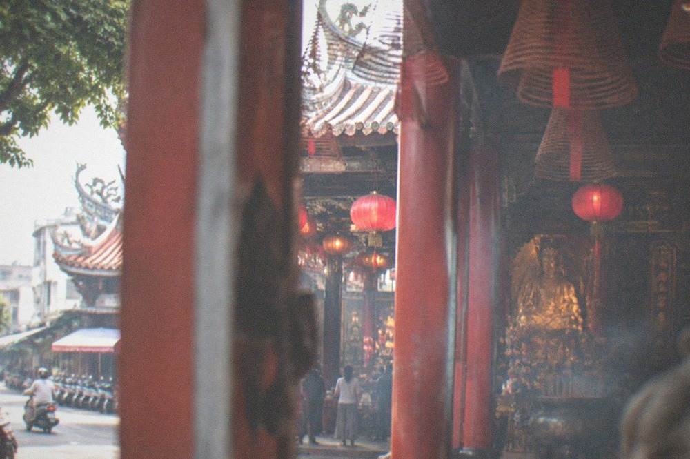 Golden statue of a seated deity inside a dimly lit temple hall with red lanterns and carved woodwork