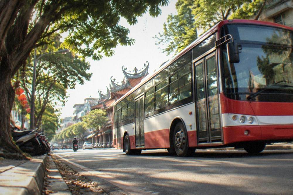 A red and white city bus at a stop on a tree-lined Tainan street