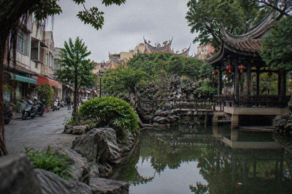 A stone-edged garden pond in Tainan reflecting a pavilion and greenery