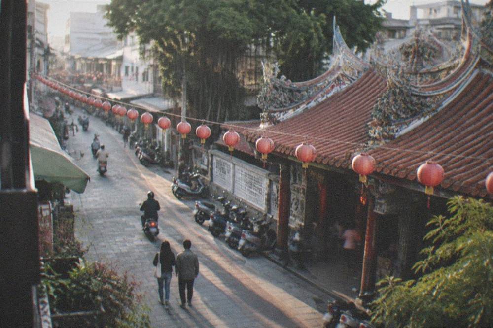 A small-town temple roofline at dusk with lanterns strung overhead