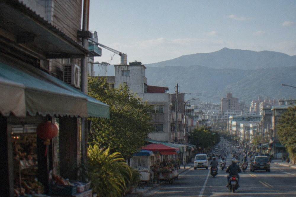 A view over a Taiwanese city skyline with low buildings and distant forested mountains under a blue sky