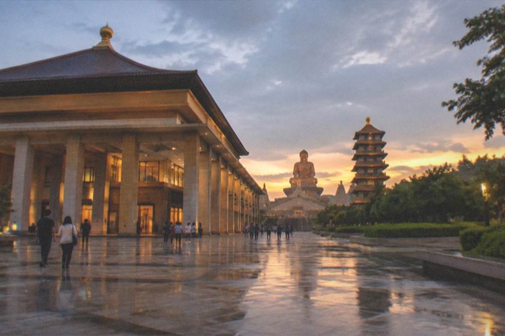 The exterior of a large Buddhist museum hall with a wide plaza in front at dusk