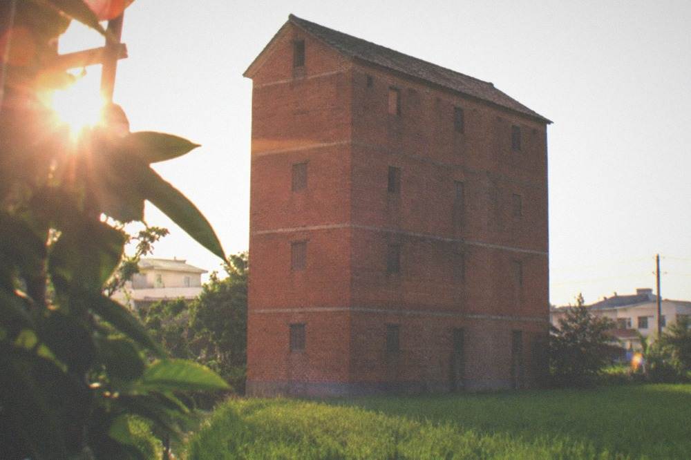 A tall red brick tobacco curing barn standing in a green field