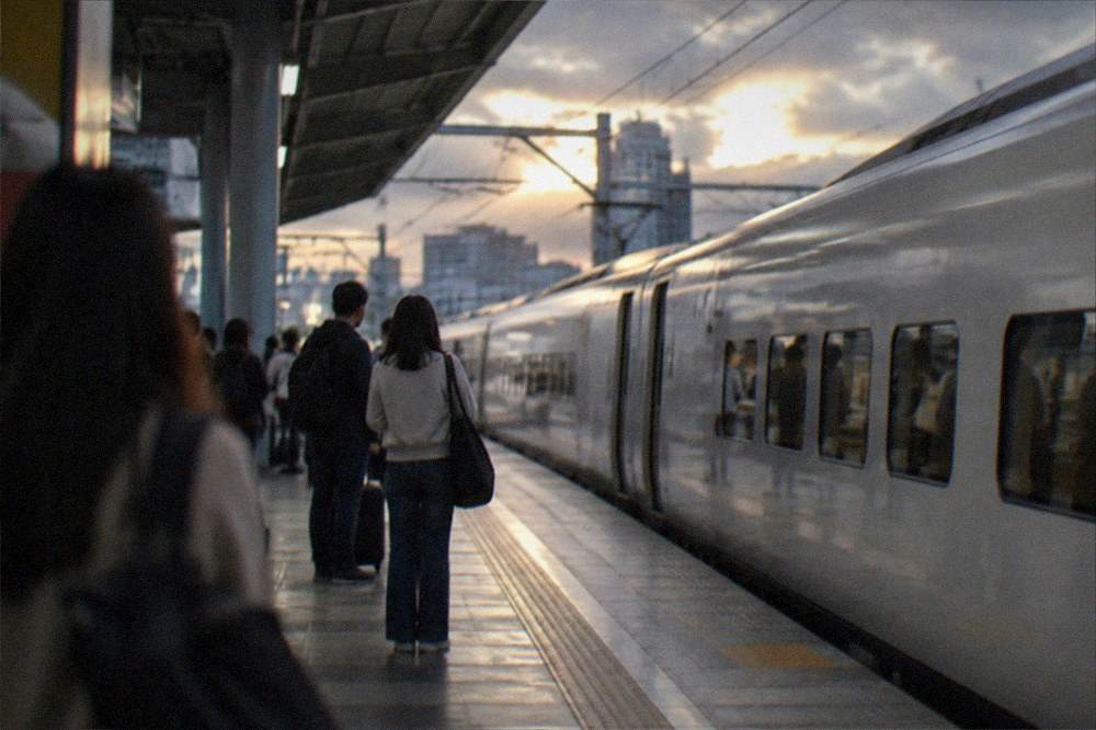 Railway platform at dusk with travelers waiting beside a sleek white train