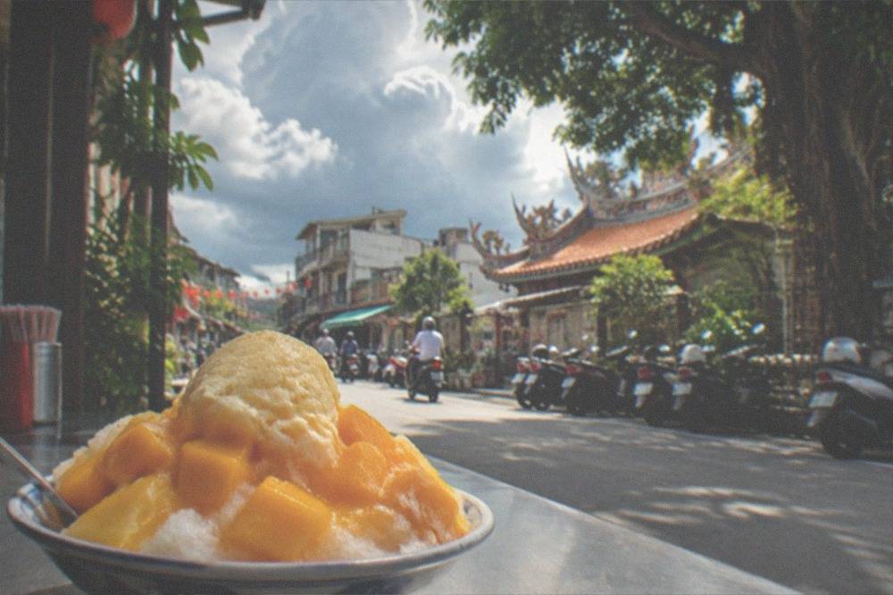 A bowl of mango shaved ice dessert with fresh mango pieces on a table