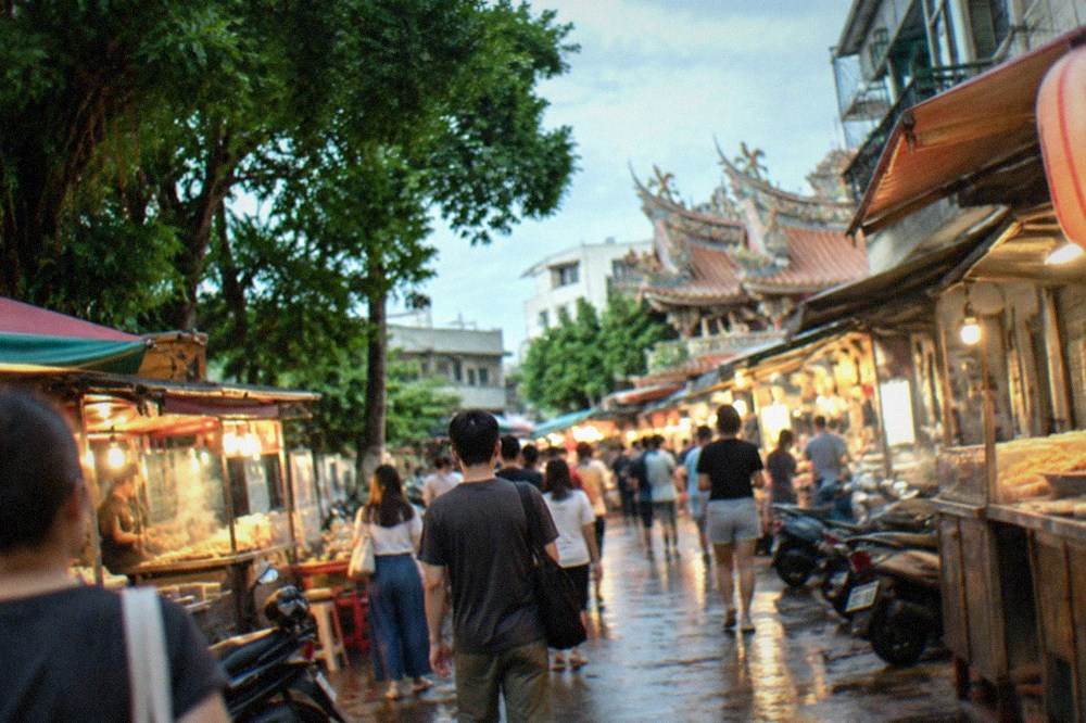 Crowded night market aisles lit by stall lights with visitors walking between food vendors