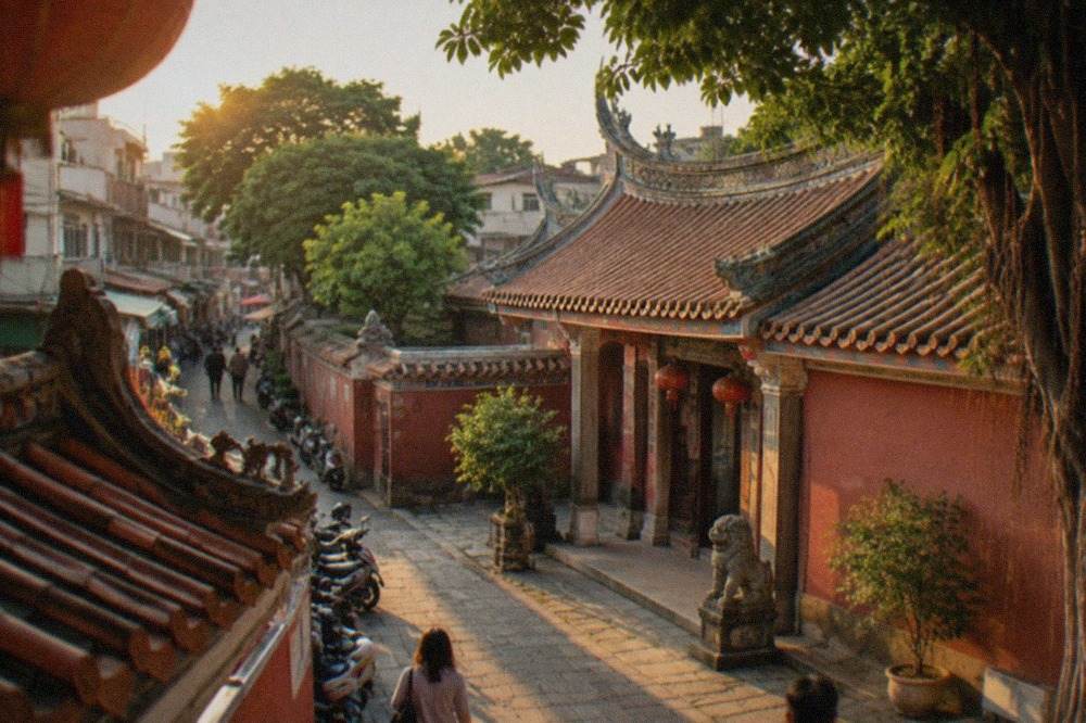 A stone archway and courtyard of an old Tainan temple with red walls and lanterns