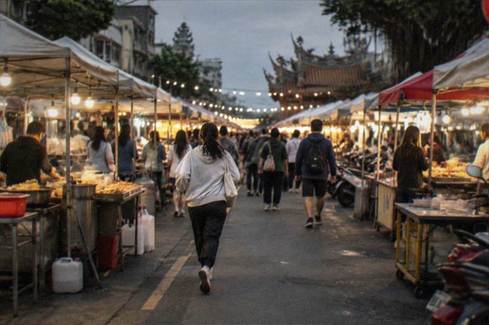 A crowded night market aisle lit by stall lights with food vendors on both sides