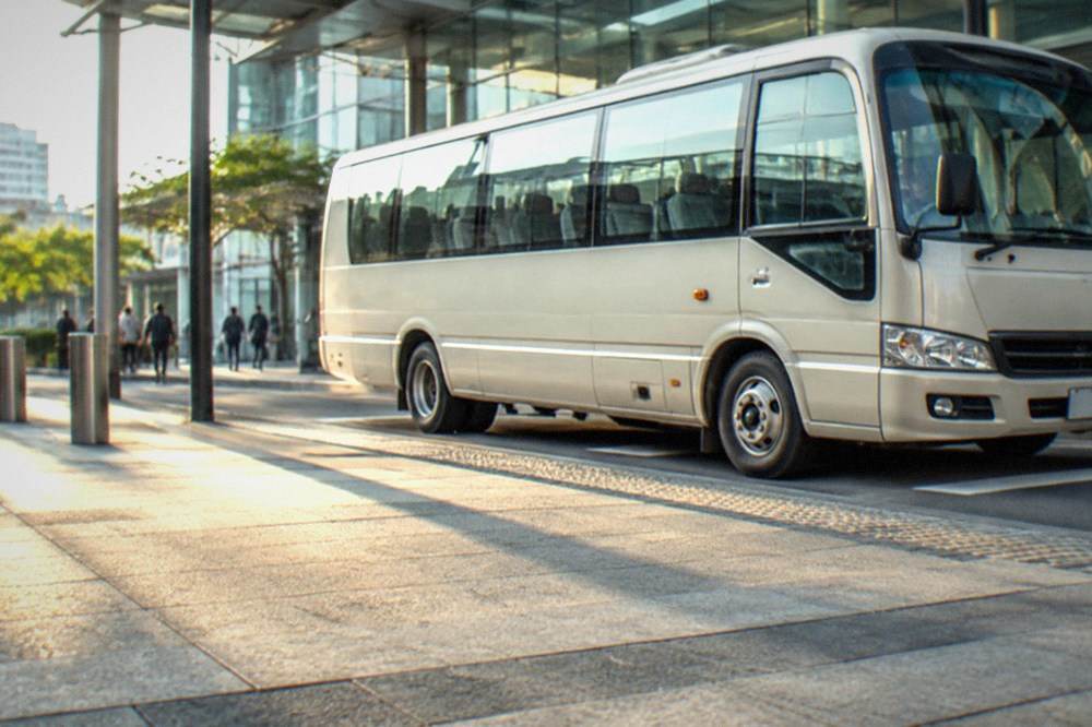 A shuttle bus parked at a station curb outside a glass station building