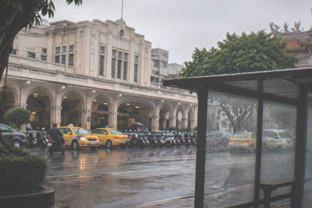Rain falling on an empty bus stop shelter with wet pavement and gray sky