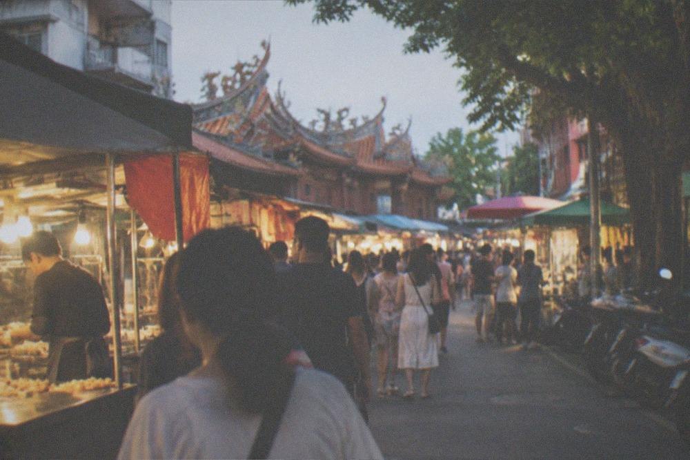 A Tainan night market aisle lit by stall lights with crowds browsing food stands in the evening