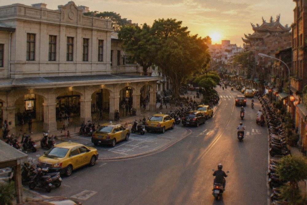 A Tainan street at dusk with old brick buildings, warm shop lights and scooters parked along the sidewalk
