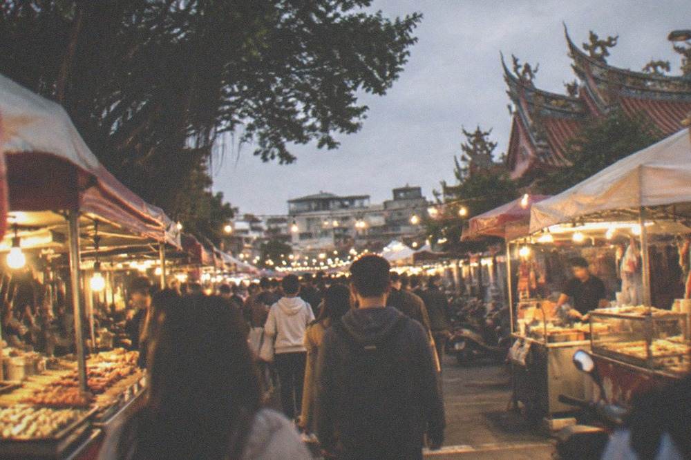 A crowded night market aisle lit by warm stall lights with food vendors on both sides