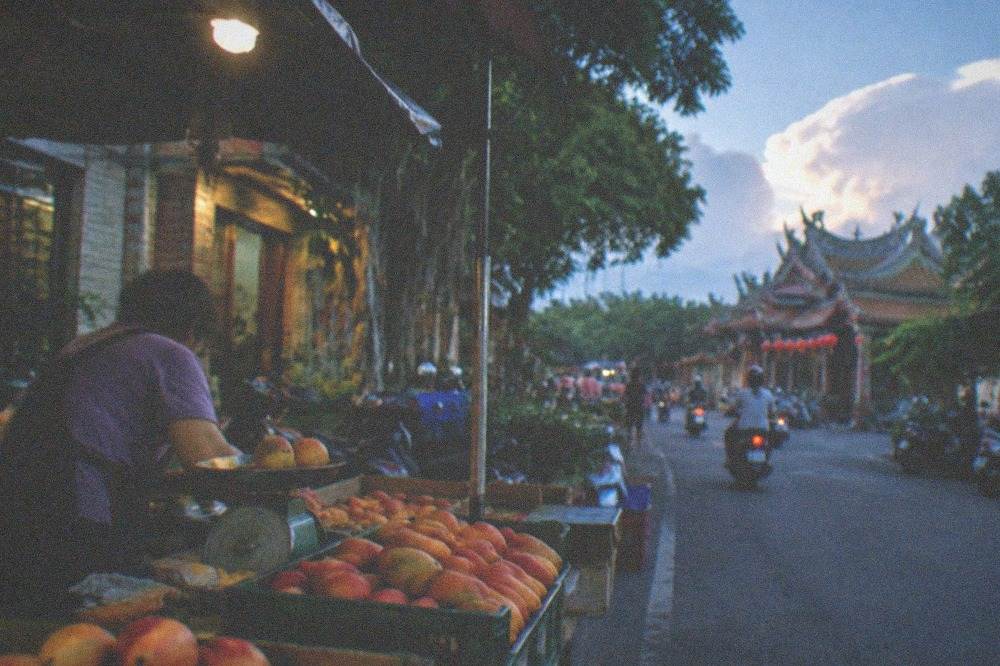 A roadside fruit stand in Yujing with boxes of mangoes and a vendor weighing fruit