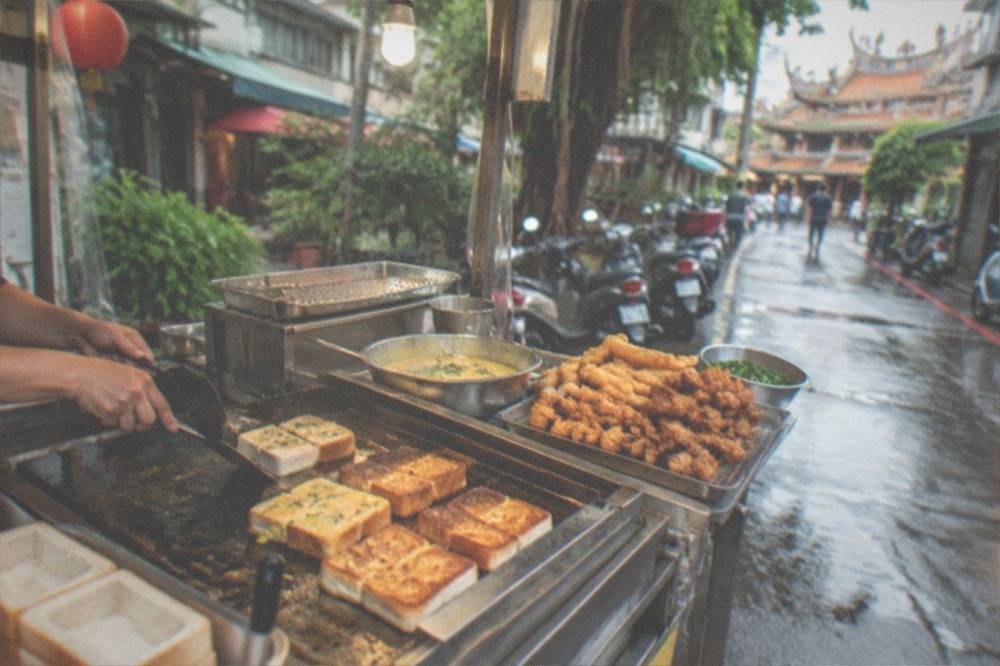 A night market griddle with coffin bread and fried snacks being prepared