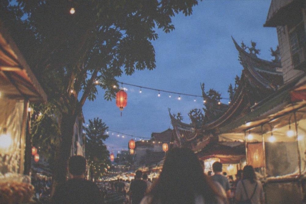 Crowds walking between food stalls under string lights at a Tainan night market