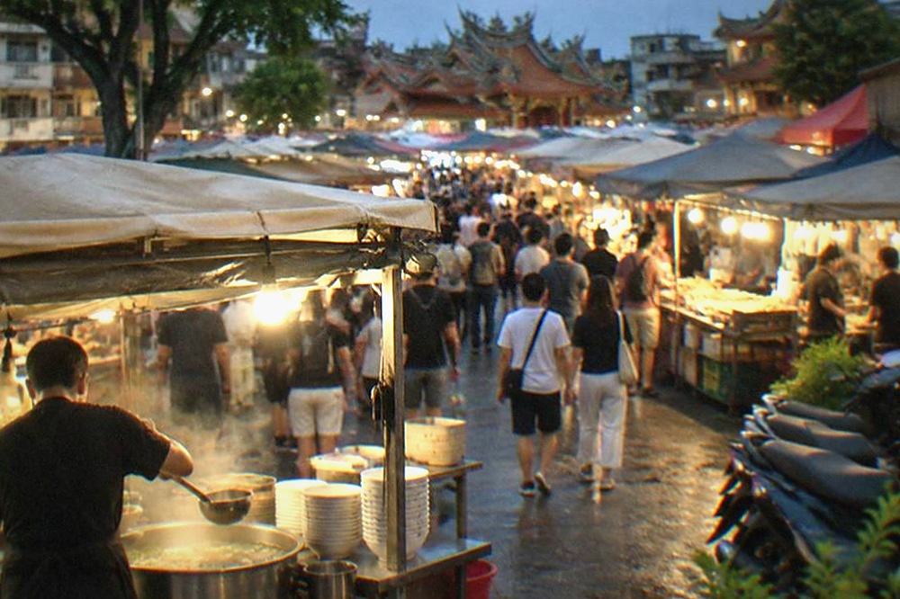 A vendor ladling soup at a night market stall, with bowls stacked beside the counter