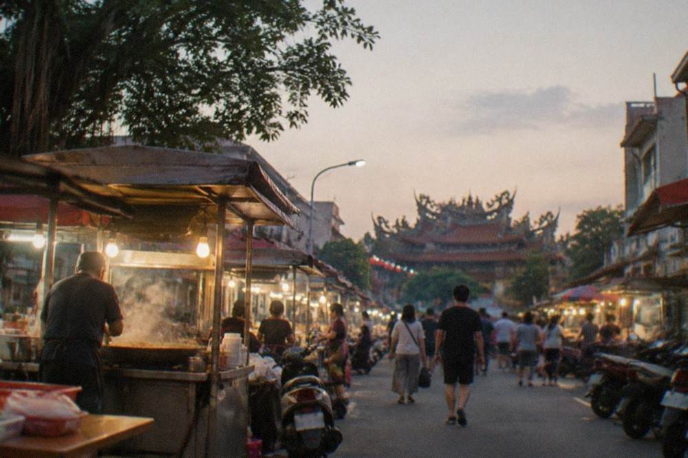Food vendors cooking at an outdoor Tainan night market under bright stall lights at dusk